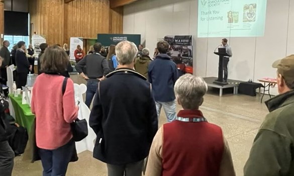 People standing watching a speaker at an event.